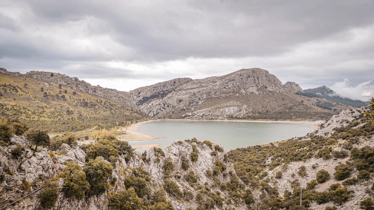 An enchanting view of the Balearic mountains, where a tranquil lake reflects the cloudy sky.