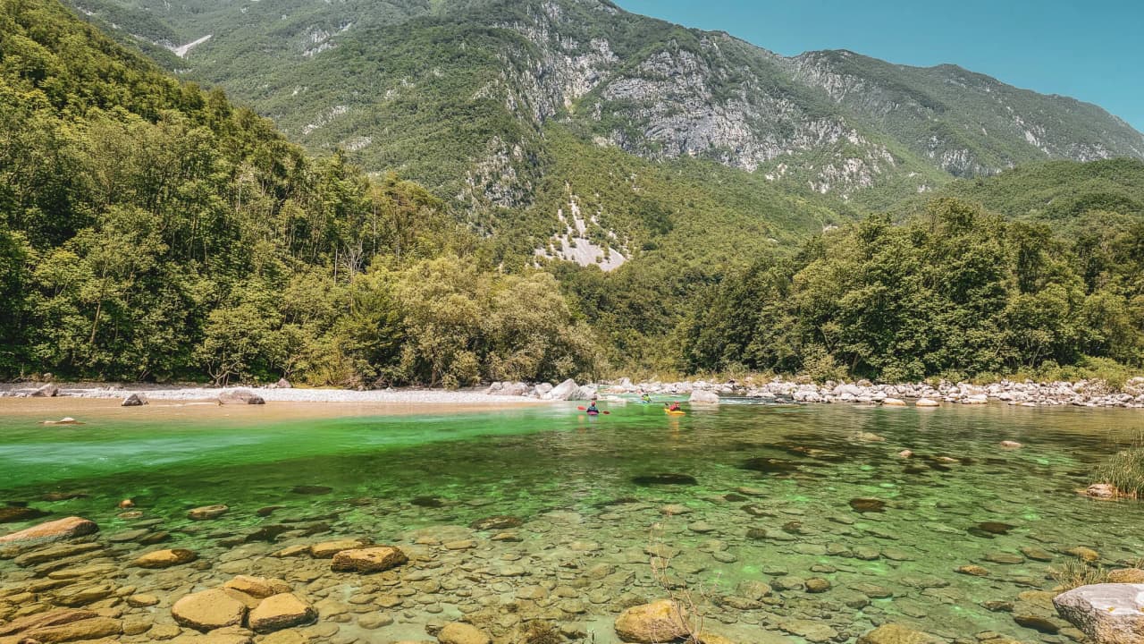A crystal-clear river with kayakers, surrounded by green mountains in Slovenia.