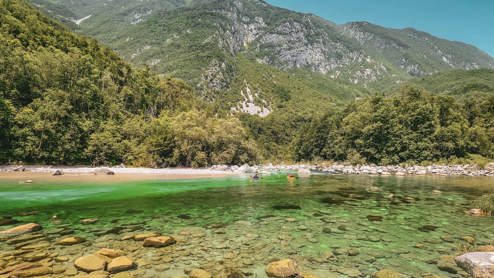 Rivière cristalline avec des kayakistes, entourée de montagnes verdoyantes en Slovénie.