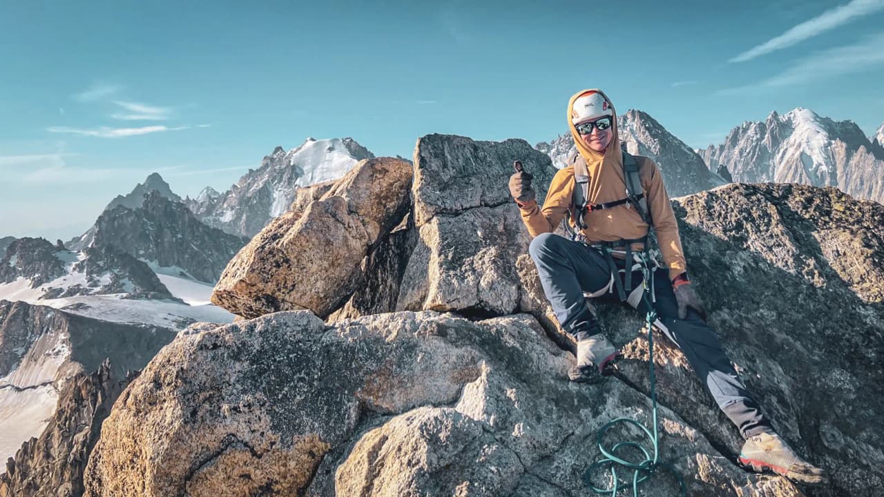 Un alpiniste sur un sommet rocheux, avec des montagnes enneigées en arrière-plan à Chamonix.