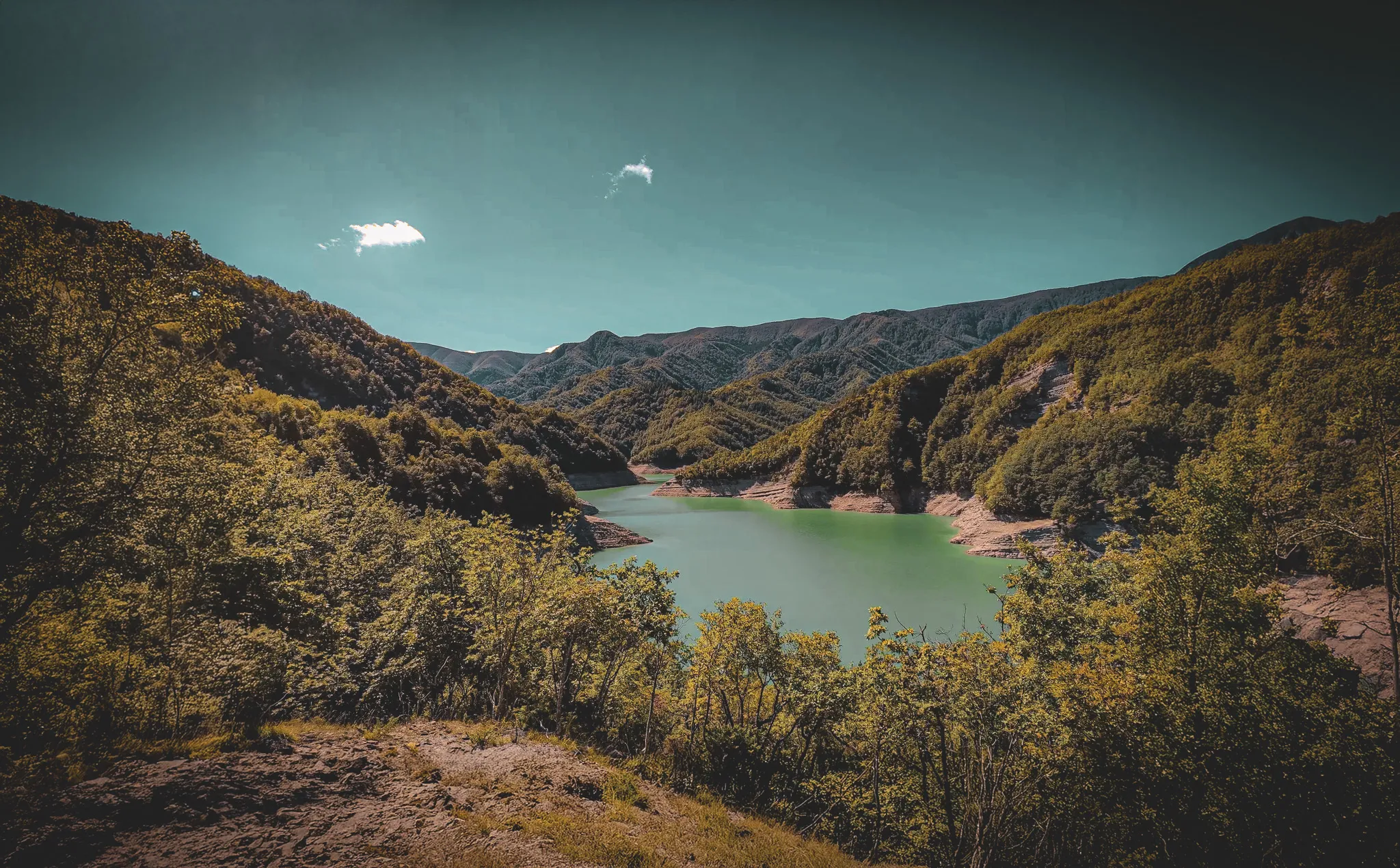 Lago Ridracoli, en Toscane, Italie. Un paysage naturel avec un lac aux eaux verdoyantes entouré de collines et de montagnes verdoyantes. Le ciel est clair, avec quelques nuages blancs flottants.