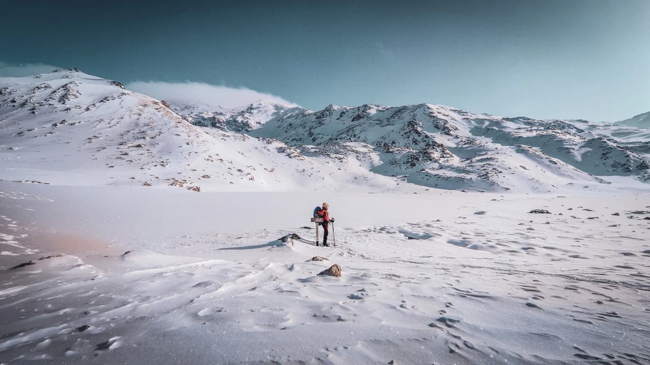 A hiker in the heart of a snow-covered landscape, facing majestic mountains beneath a blue sky.