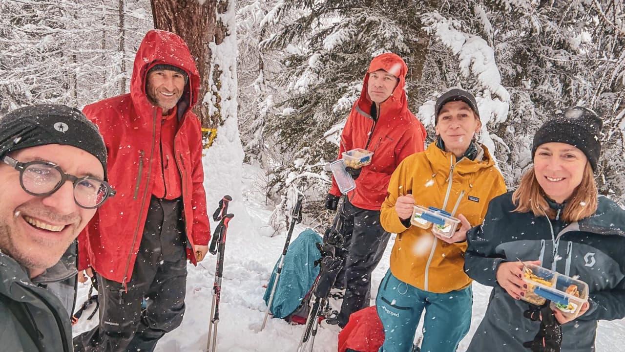 Un groupe souriant en pleine nature enneigée, savourant un repas pendant une aventure en ski de randonnée.