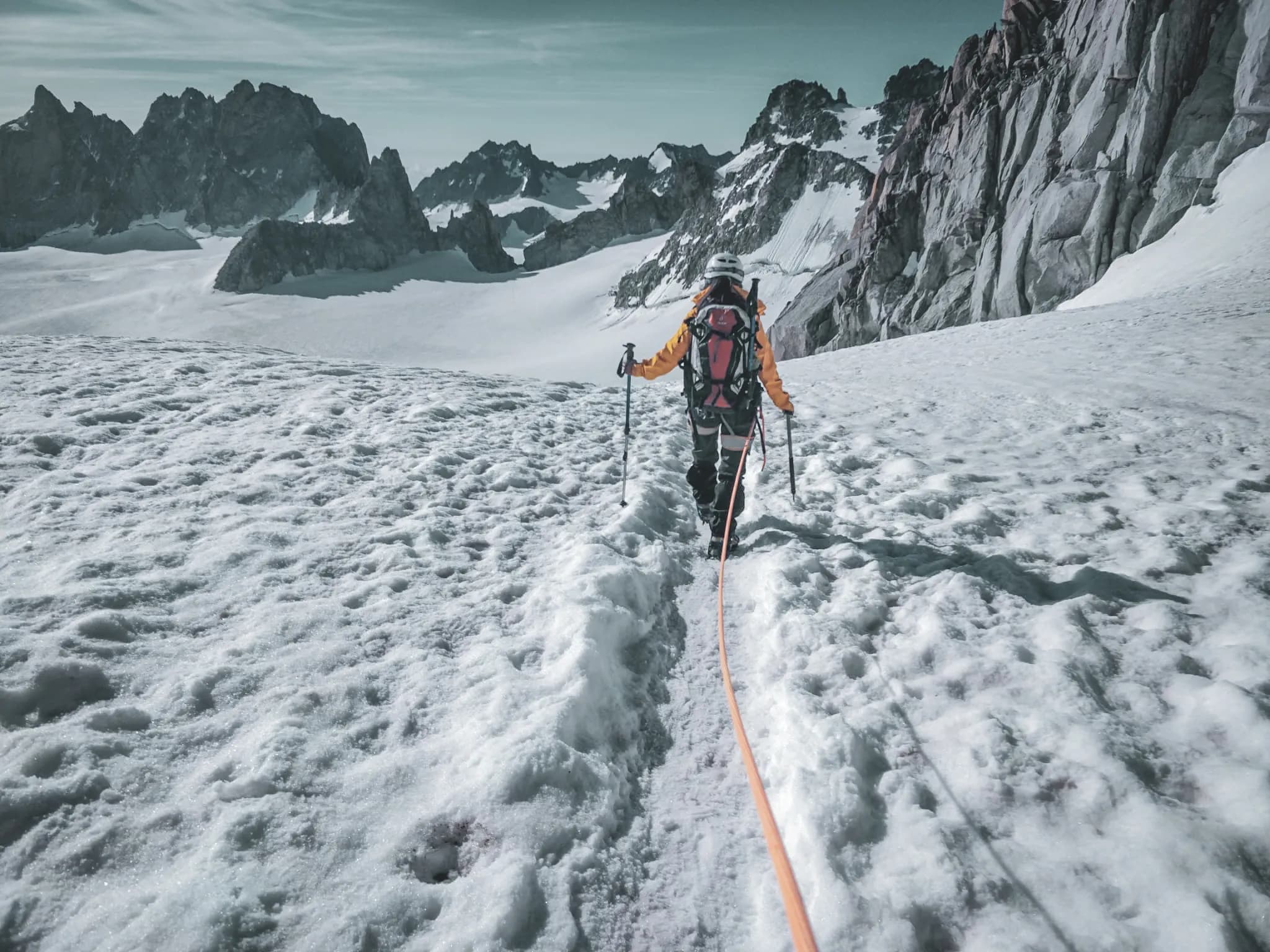 Un alpiniste sur un glacier, s'élevant vers les sommets majestueux des Alpes, sous un ciel clair.