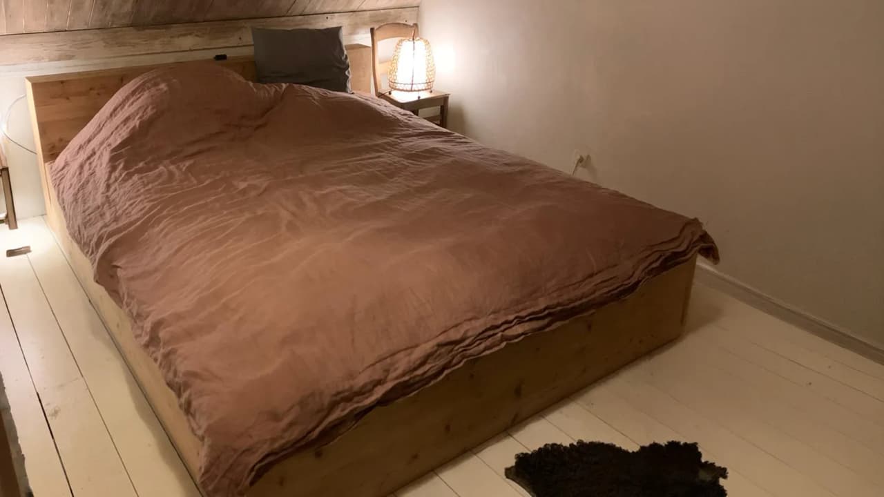 Cozy wooden room, cosy bed with pink sheets, soothing atmosphere conducive to relaxation.
