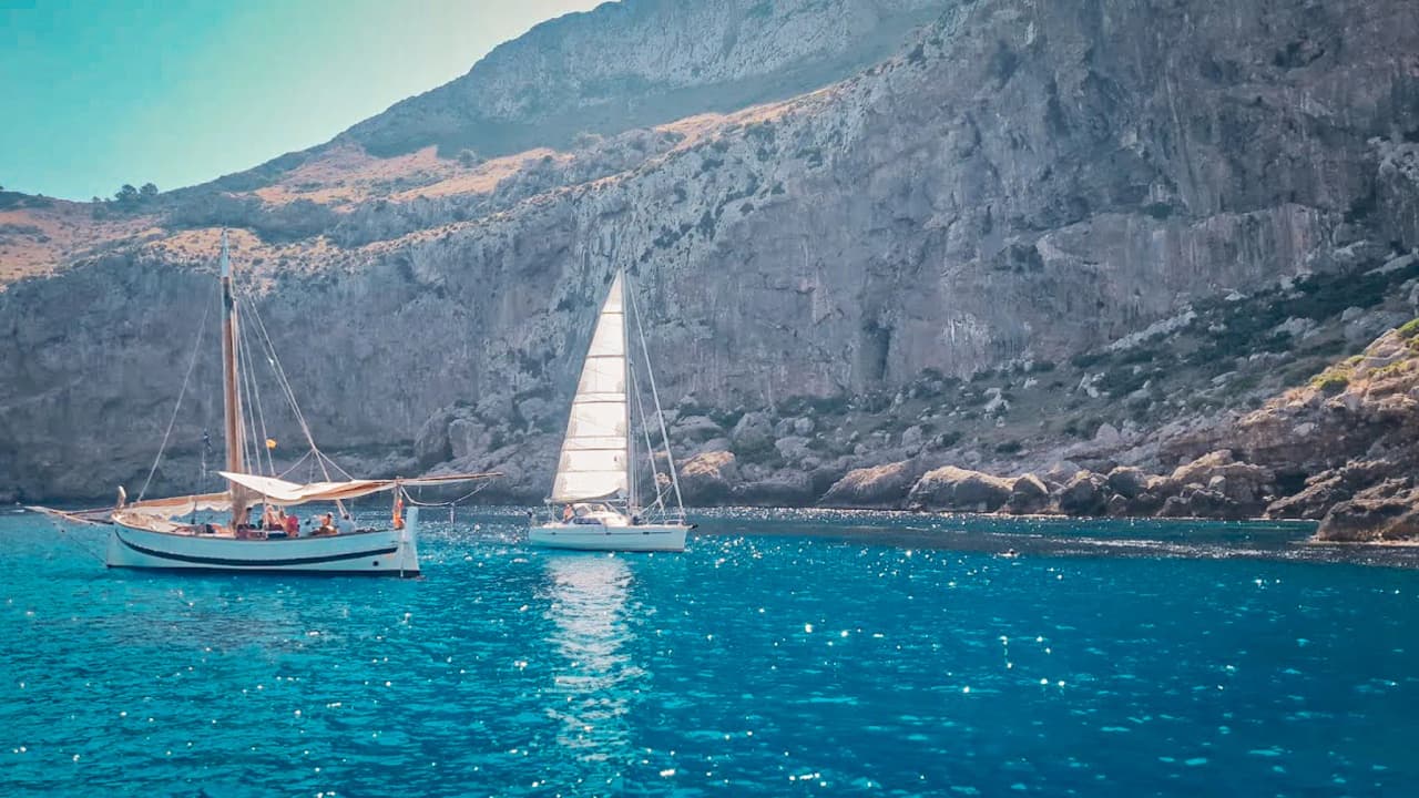 Two sailing boats are sailing peacefully amongst the sun-drenched coves of the Balearic Islands.
