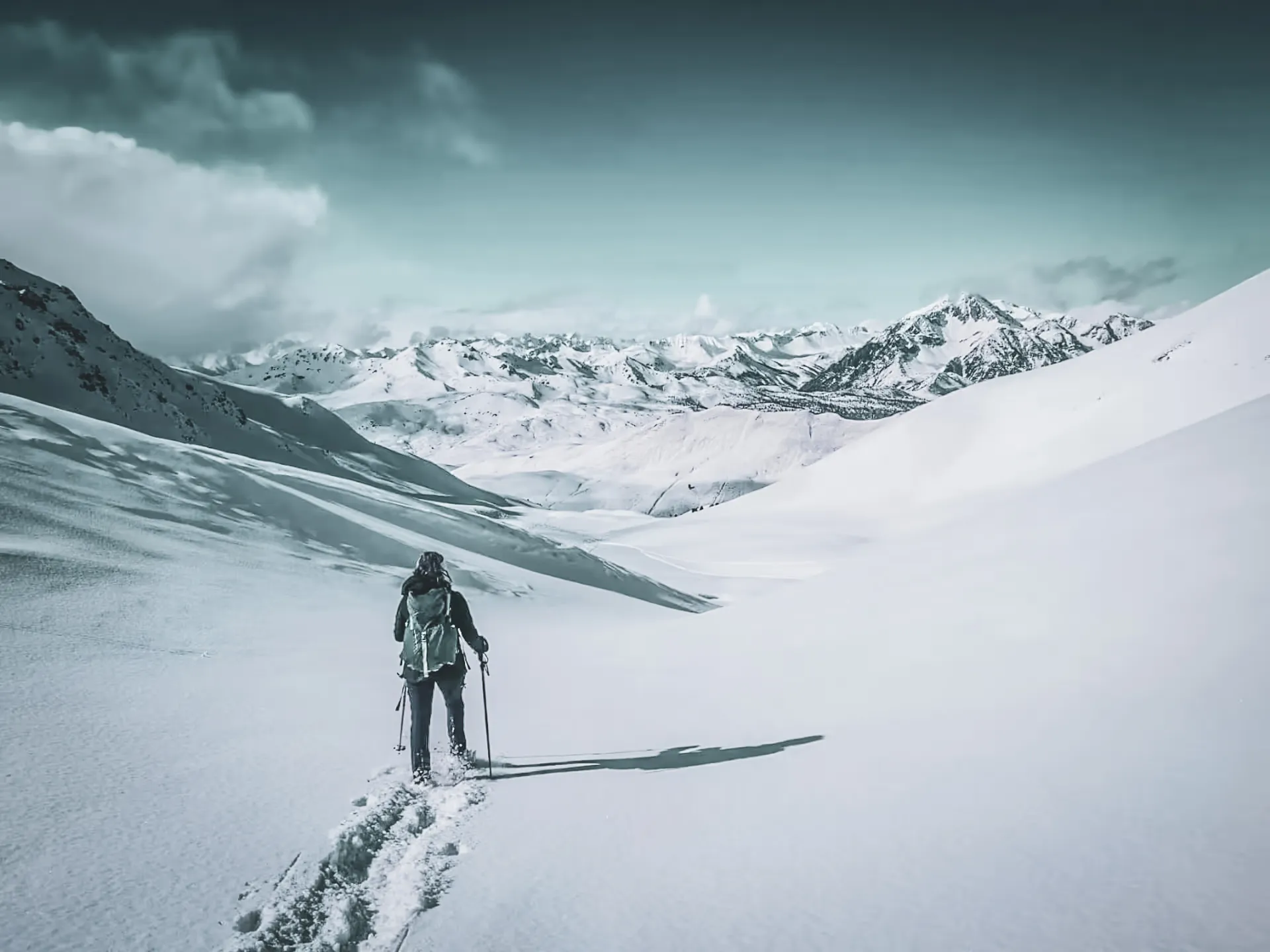 A solitary hiker traversing a snow-covered alpine landscape, past majestic peaks.