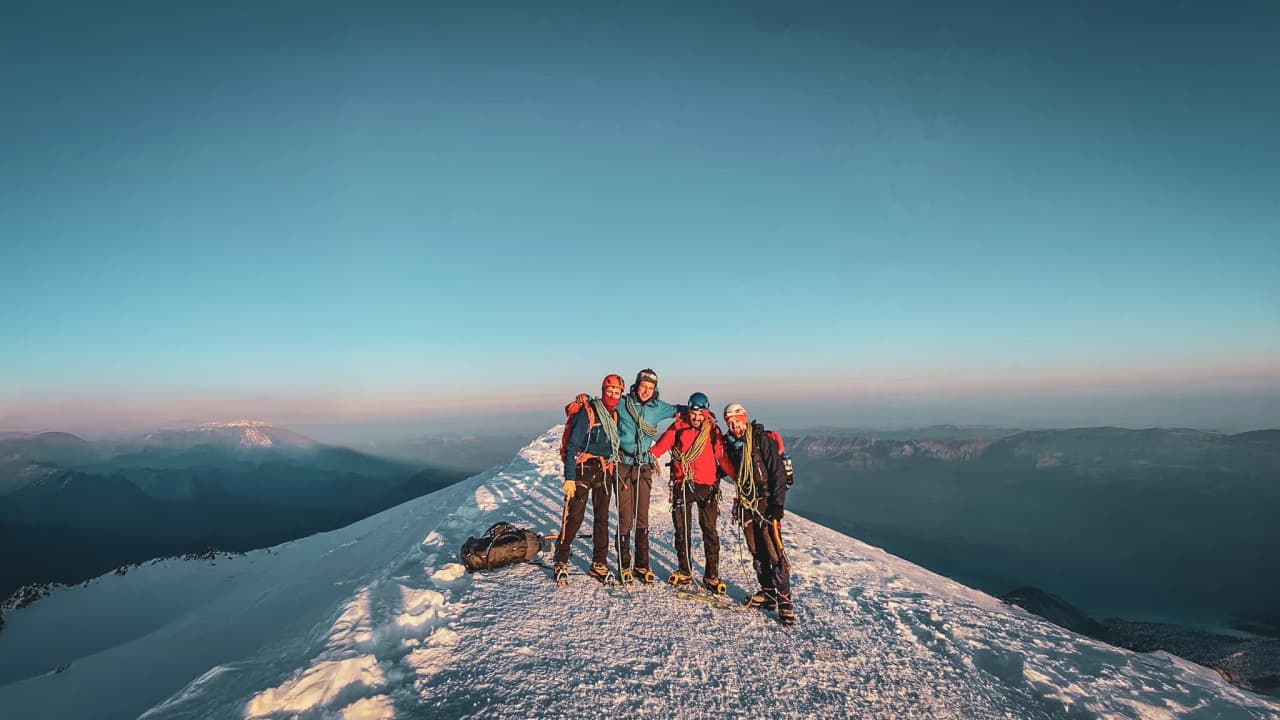 Vijf lachende klimmers op de top van de Mont Blanc, omringd door majestueuze landschappen.