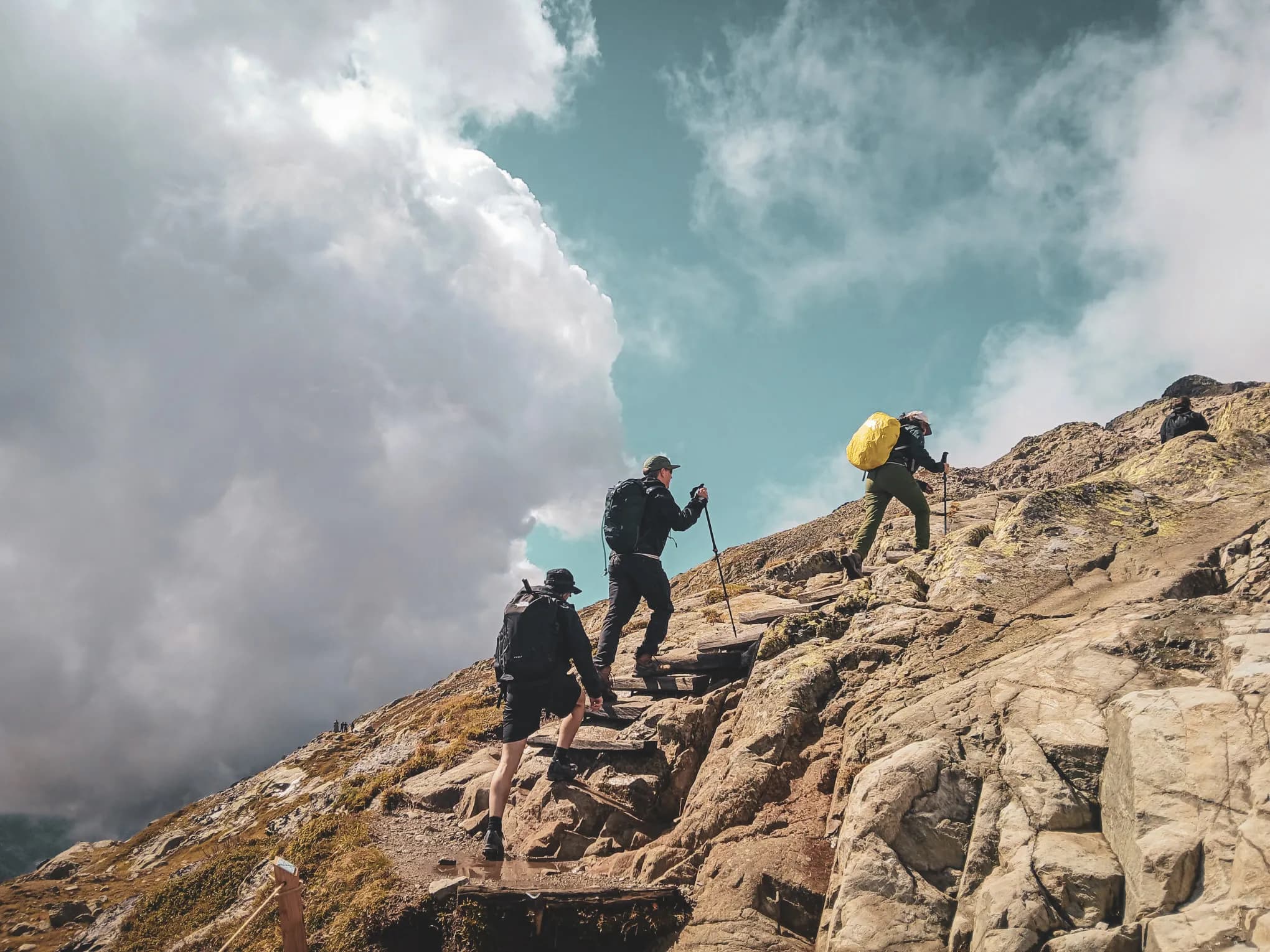 Drie wandelaars beklimmen een bergpad, omringd door majestueuze Alpenlandschappen.