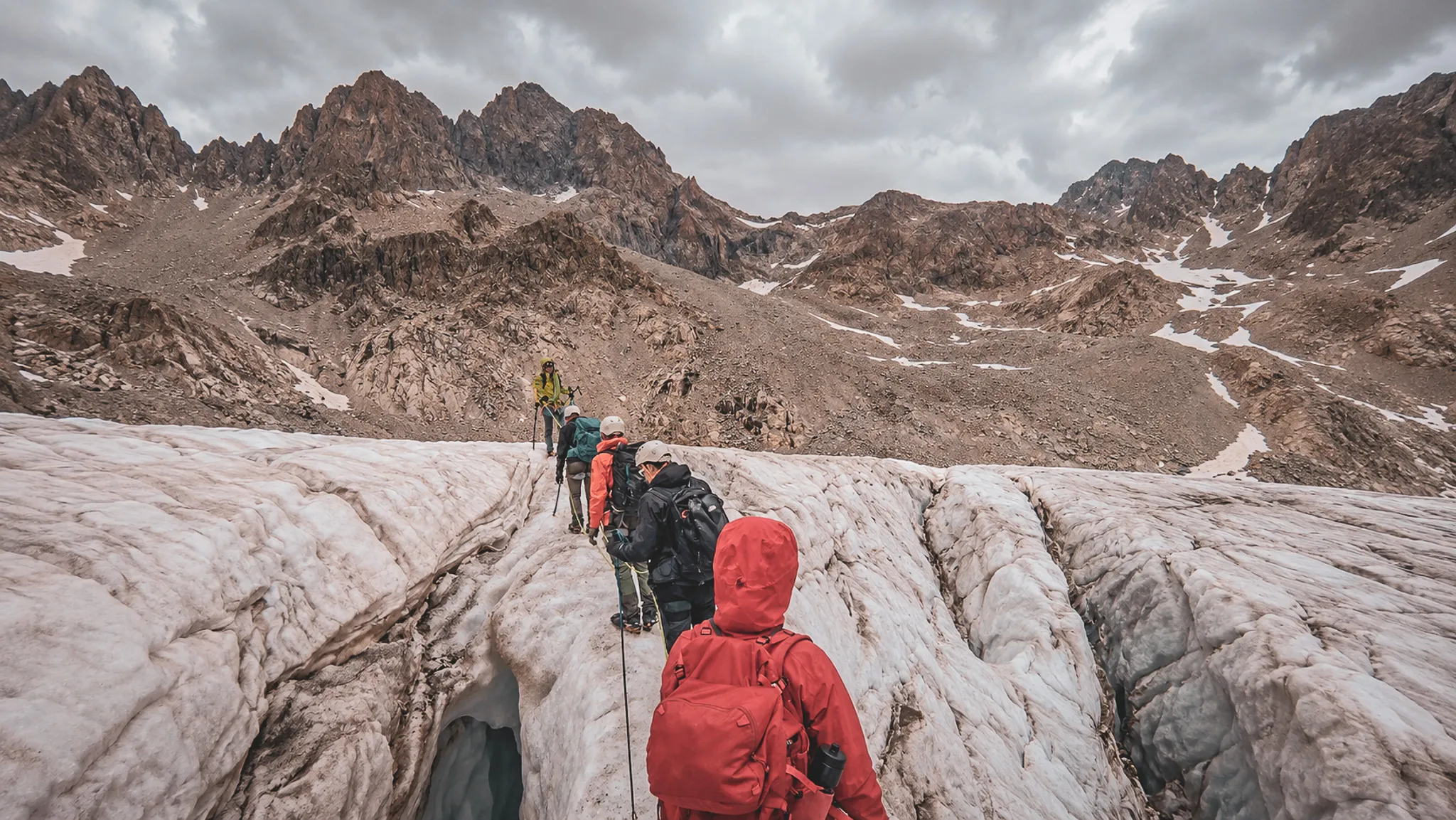 Groupe d'alpinistes traversant un glacier majestueux dans les Écrins, sous un ciel nuageux.