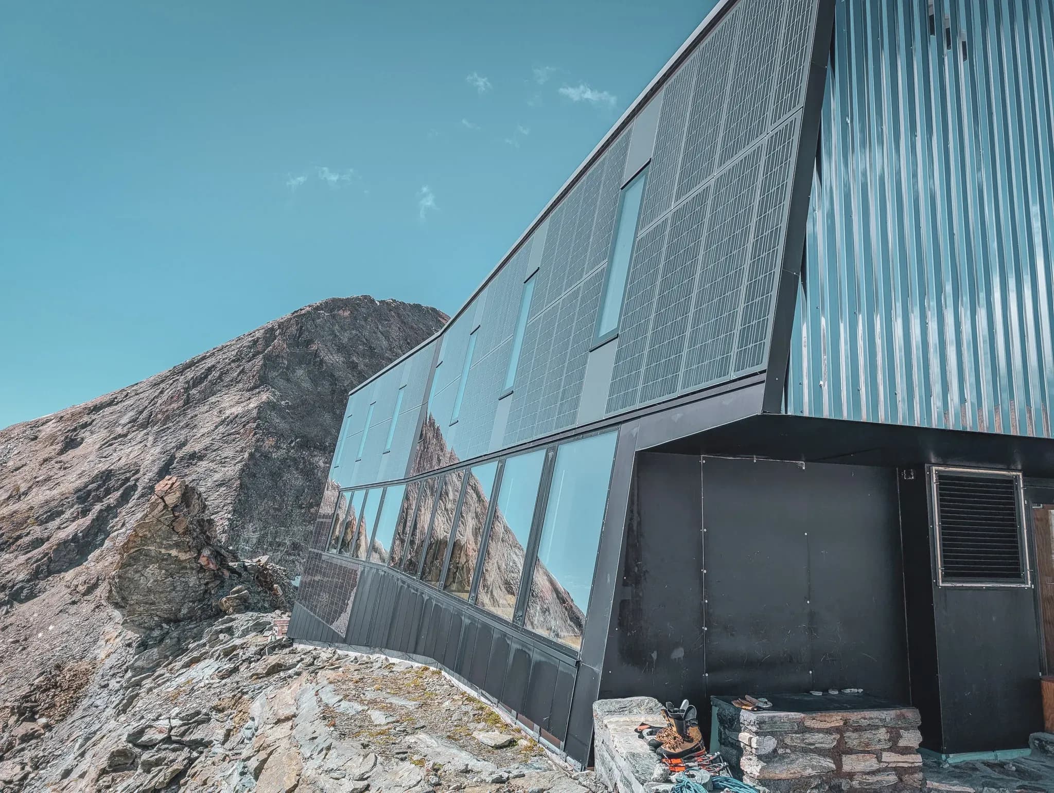 A modern mountain hut, surrounded by majestic rocks under a brilliant blue sky.