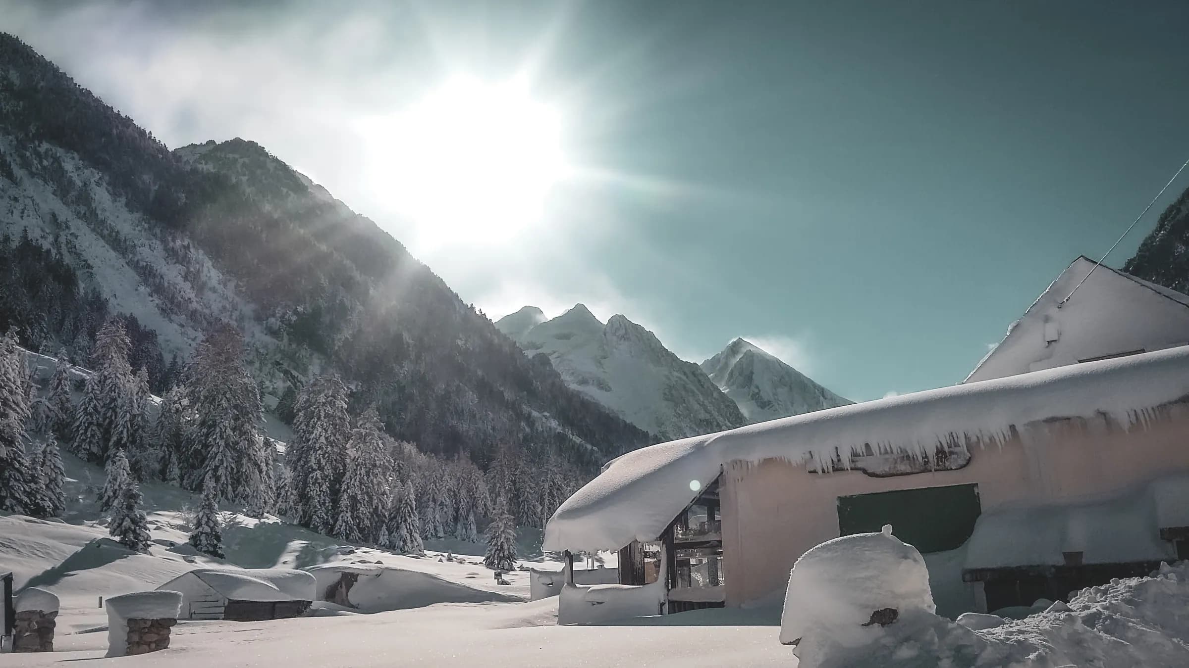 A snow-covered mountain landscape, with a cosy chalet in bright sunshine.