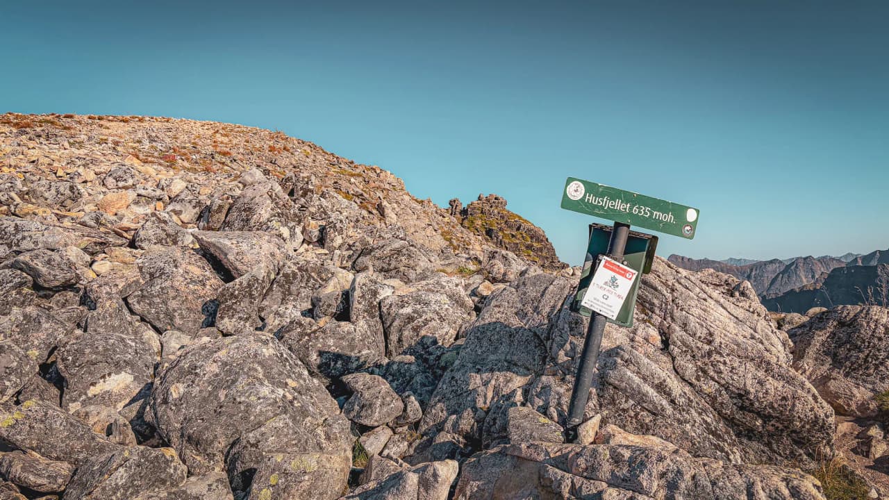 De rotsachtige top van Husfjellet op 635 m, omgeven door majestueuze landschappen en een stralend blauwe lucht.