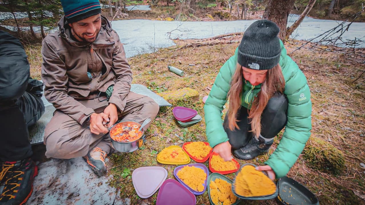 Deux personnes en pleine nature préparent un repas coloré, entourées par la forêt du Vercors.
