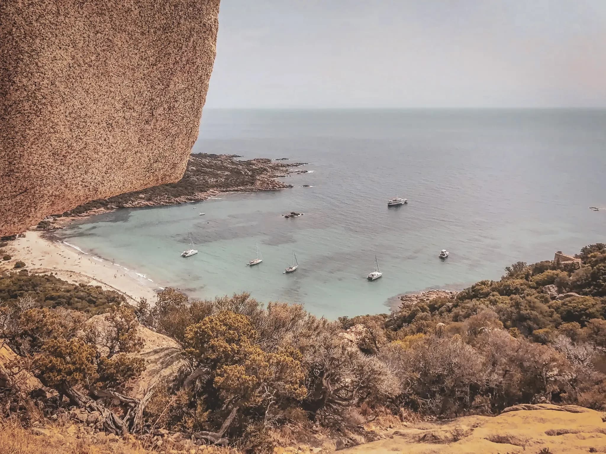 Vue panoramique sur une crique turquoise, avec des voiliers ancrés près d'une plage pittoresque.