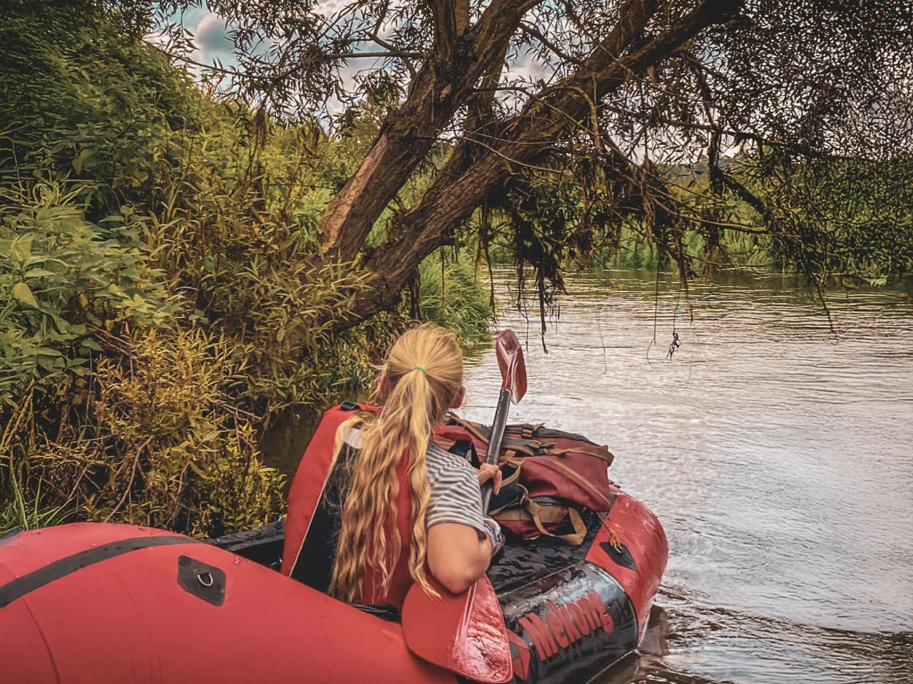 One person on a packraft explores a peaceful river lined with lush greenery.