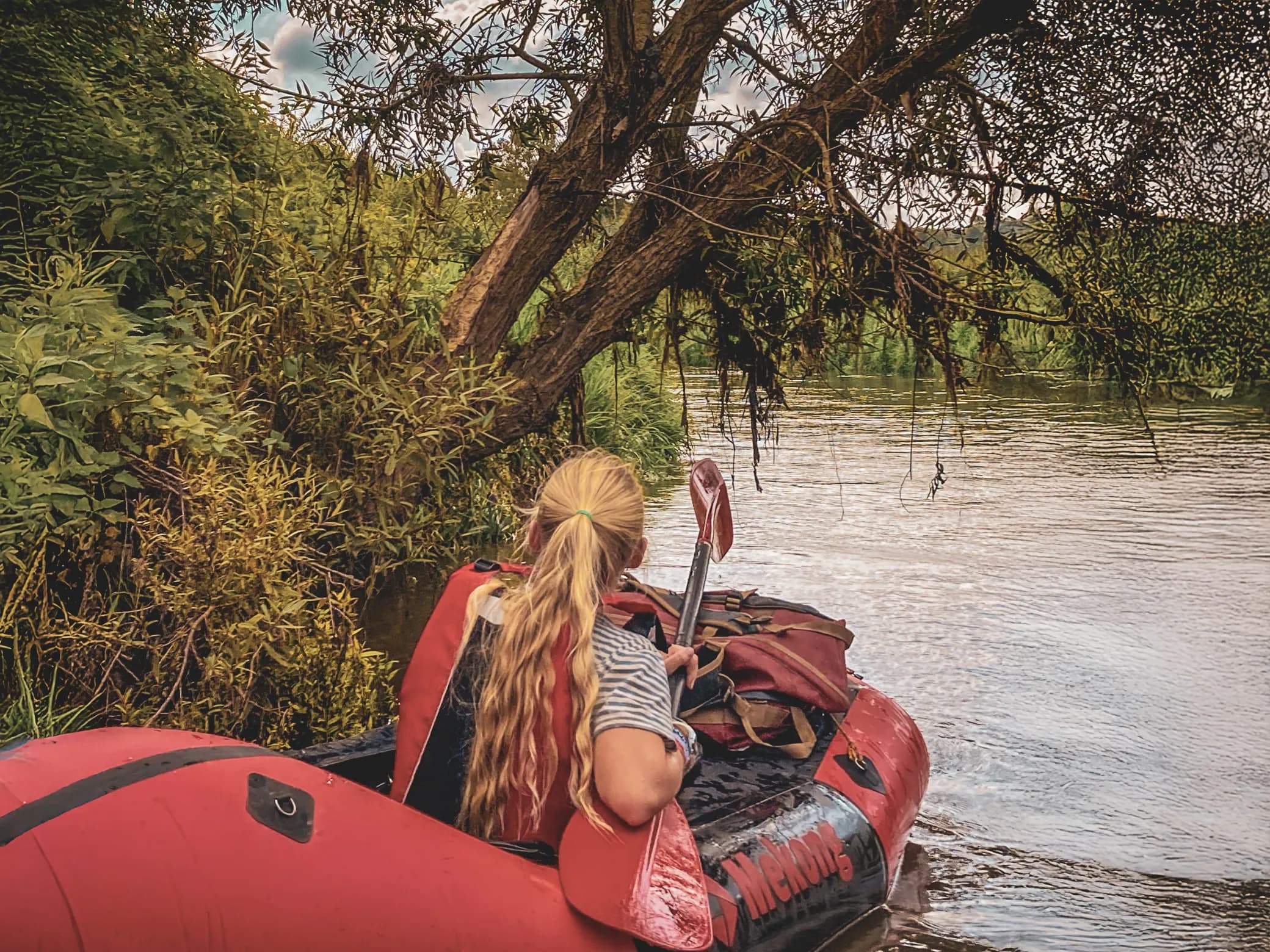 One person on a packraft explores a peaceful river lined with lush greenery.