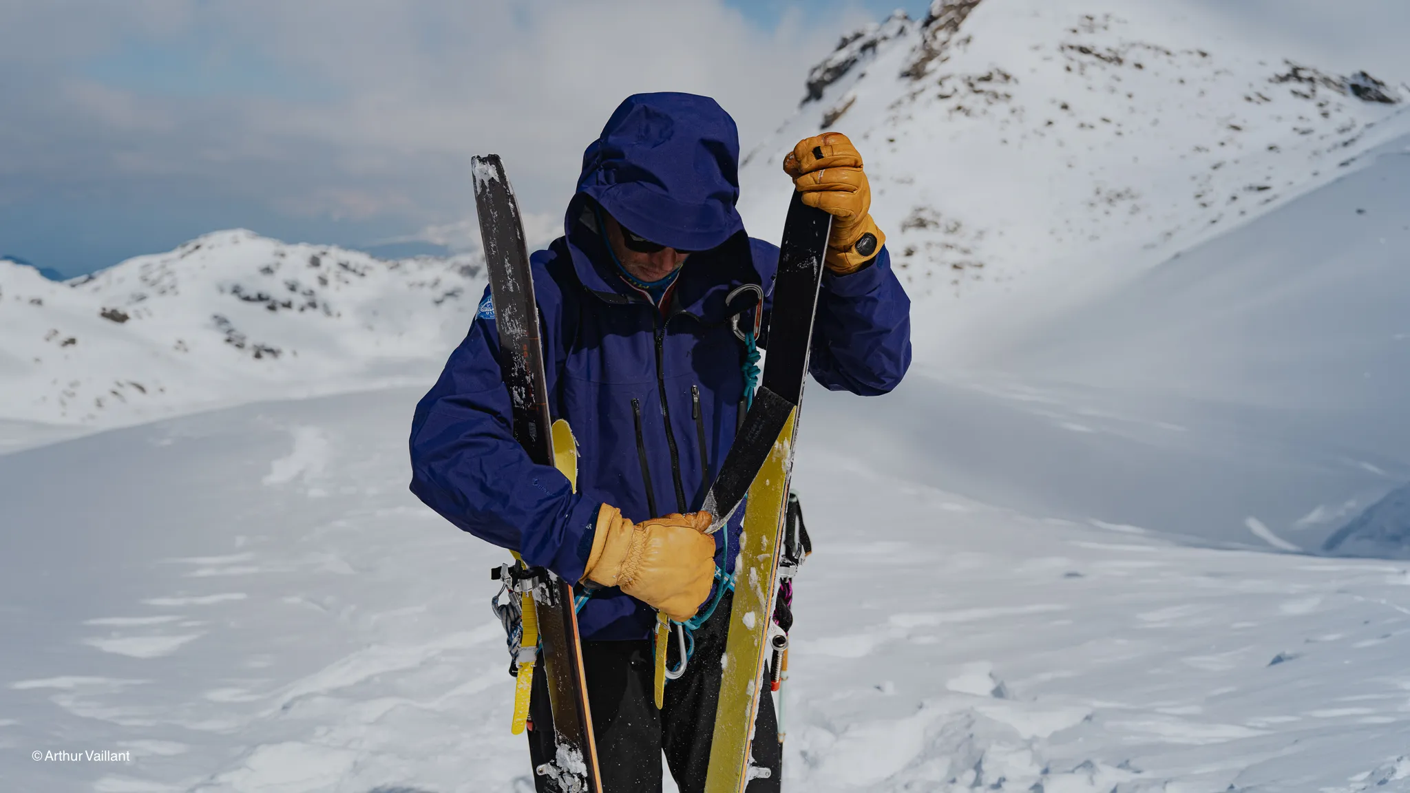 A skier gets his kit ready at the summit of the Alps, against a backdrop of breathtaking snow-covered landscapes.