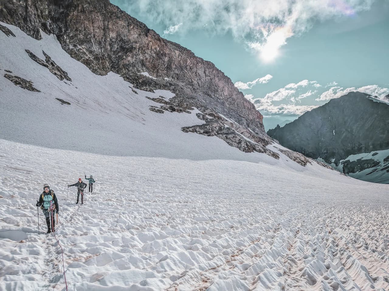 Three mountaineers make their way across a pristine glacier under a sunny sky in the Ecrins mountains.