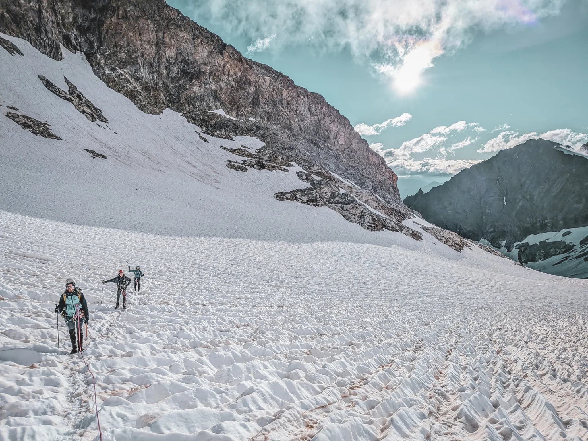 Three mountaineers make their way across a pristine glacier under a sunny sky in the Ecrins mountains.