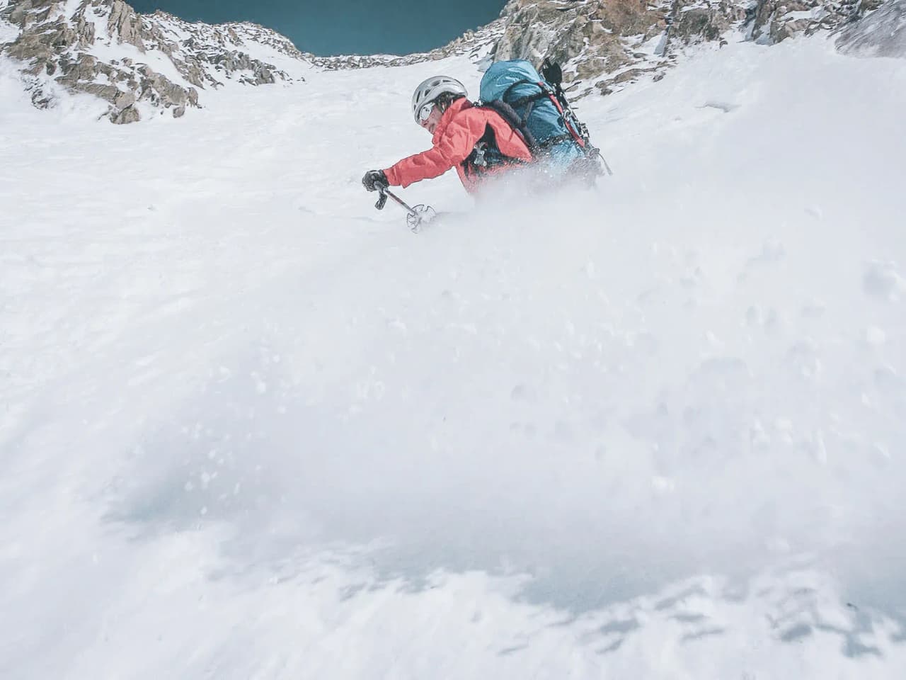 Un skieur dévale une pente glaciaire, éclaboussant des flocons de neige sous un ciel bleu.