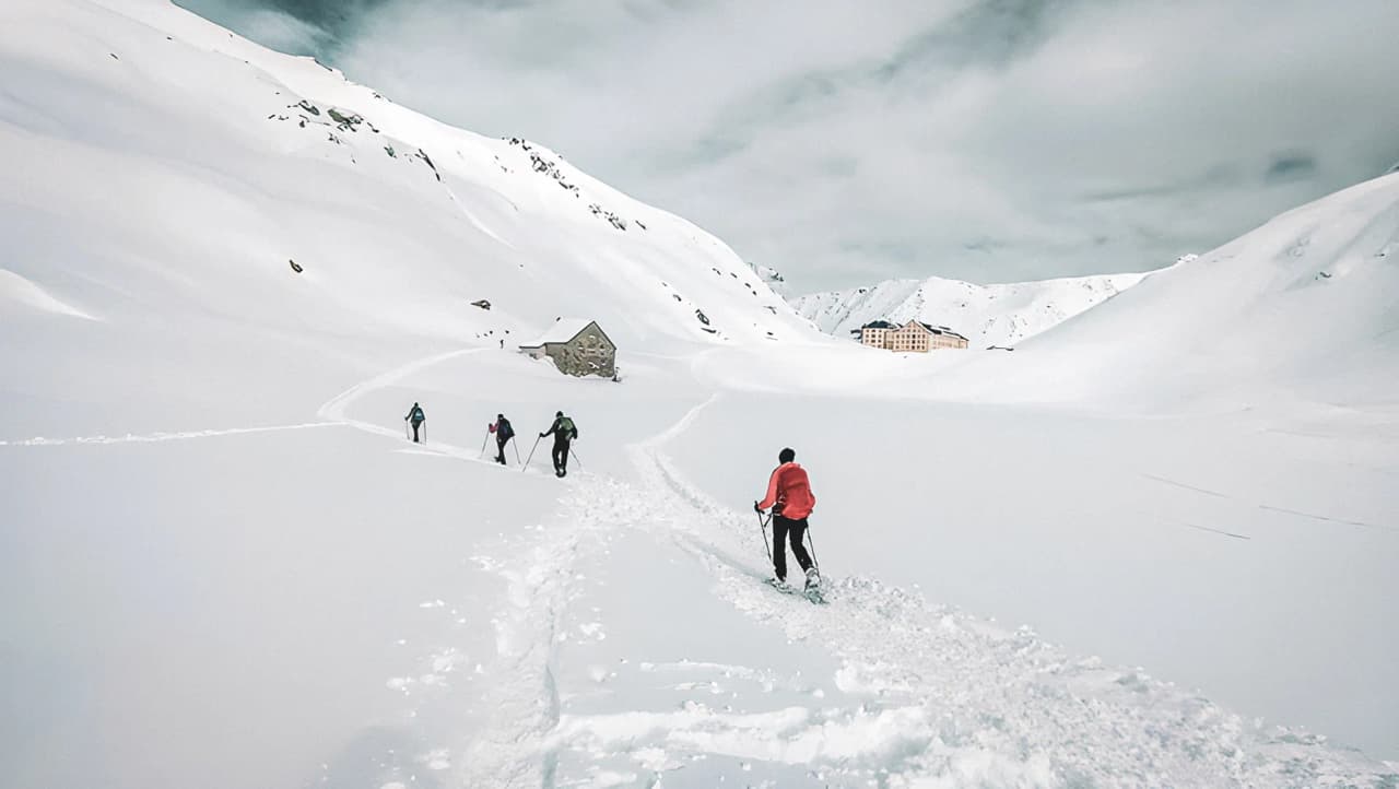 Groupe de randonneurs en raquettes, traversant des paysages enneigés vers l'hospice.