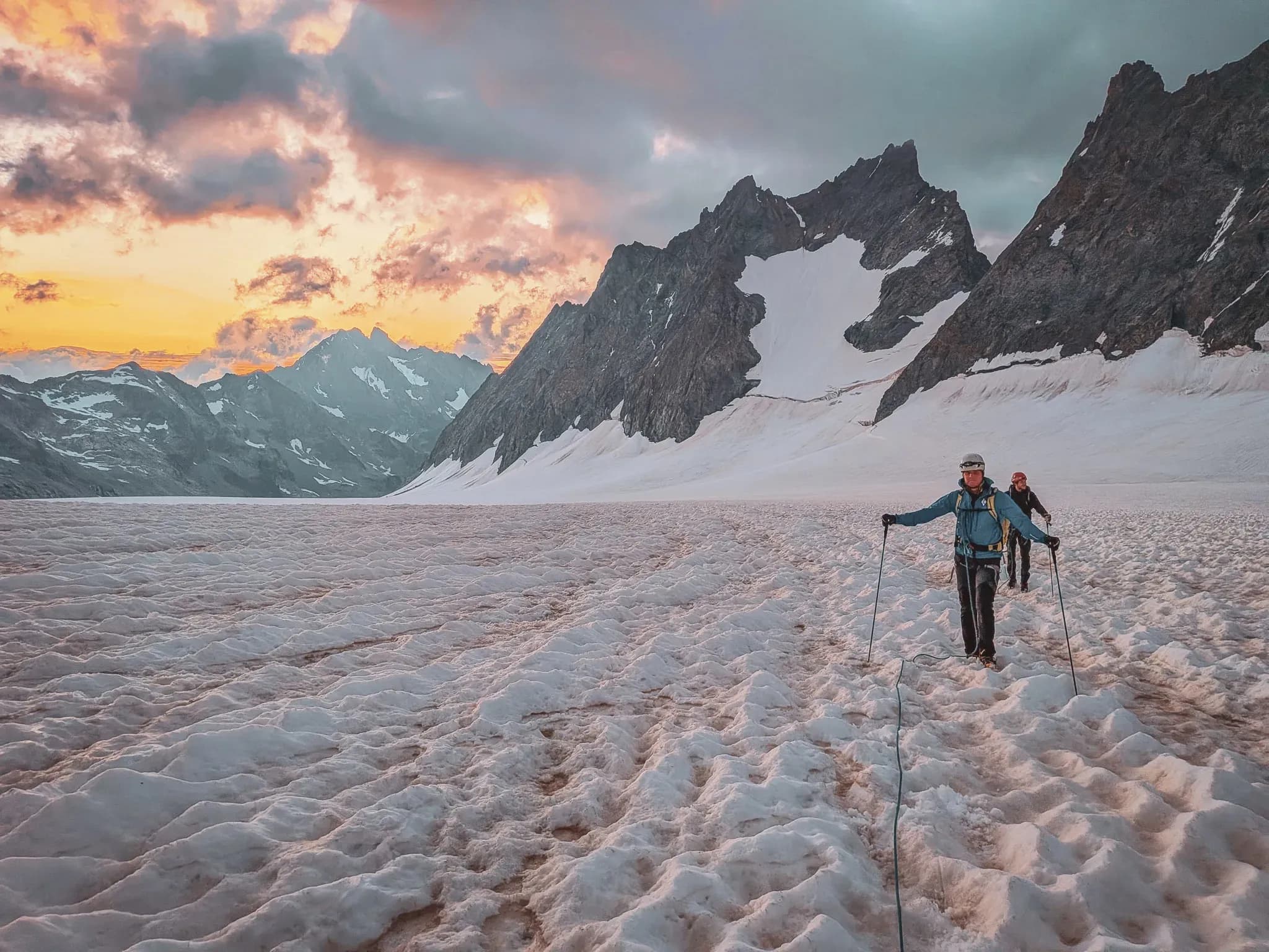 Hikers on a glacier, majestic mountains and a dazzling sunset.