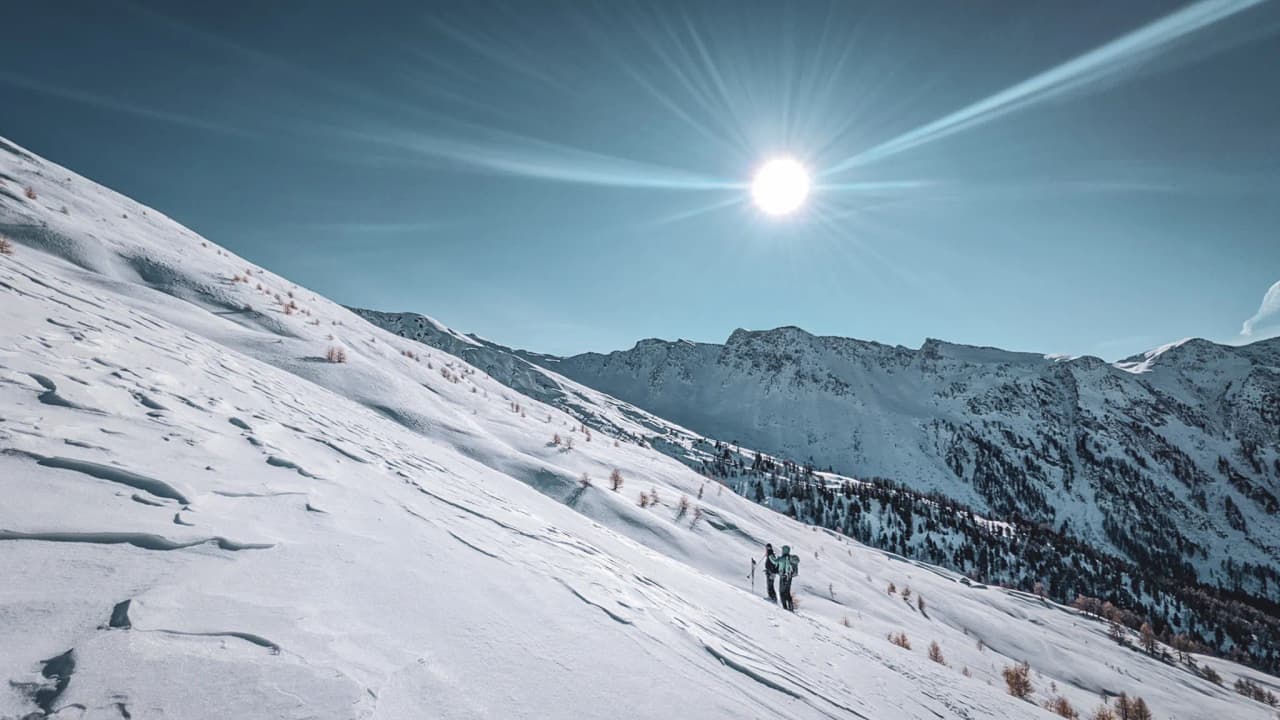 Un paysage enneigé du Queyras, avec des skieurs découvrant la beauté alpine sous le soleil.