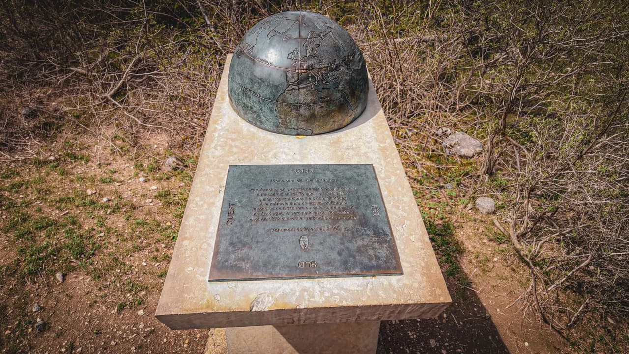 Monument en bronze représentant une carte du monde, entouré de la nature verdoyante du Vercors.