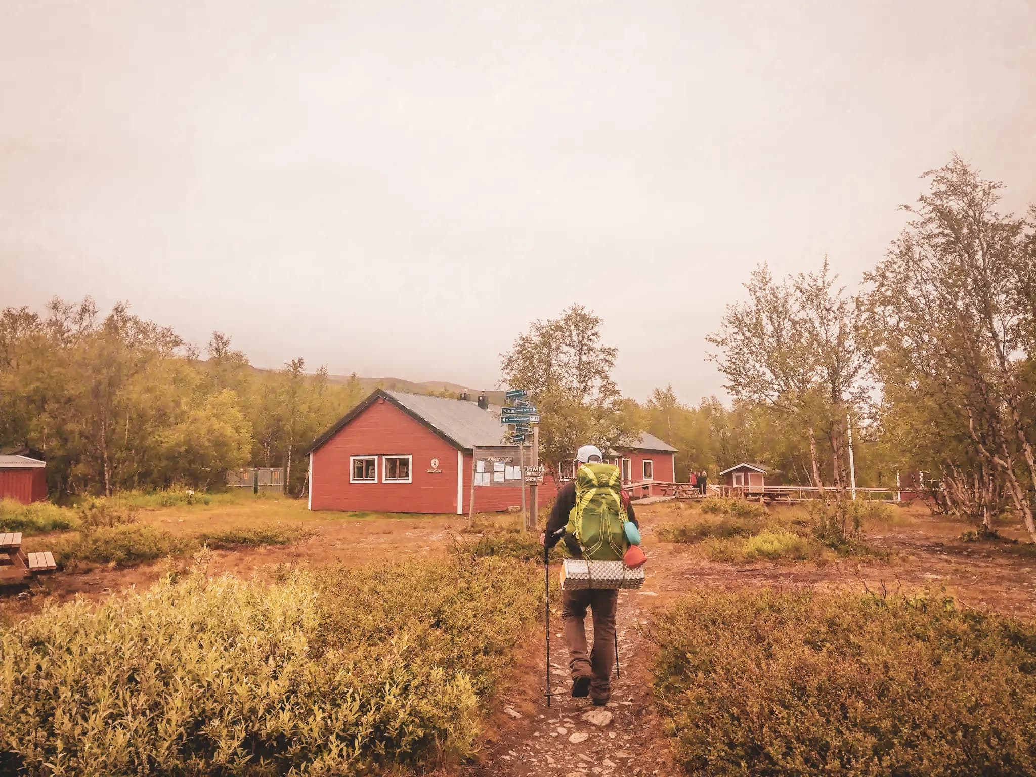 Hiker with a big bag explores the path to picturesque chalets in Swedish Lapland.