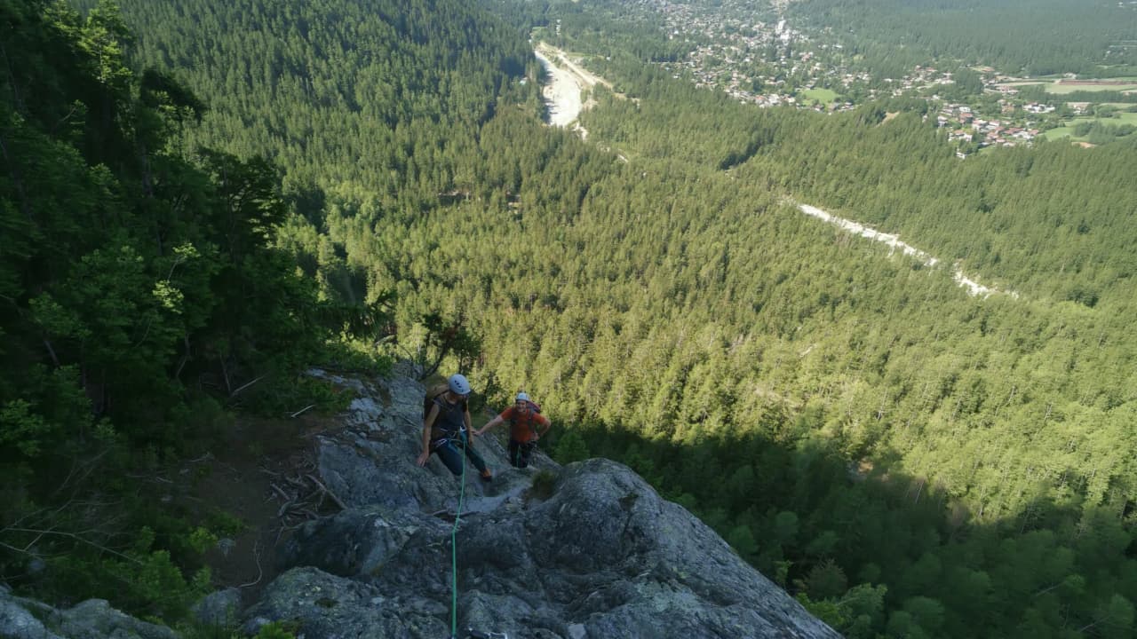 Two climbers make their way up a rocky ridge, with a panoramic view of the green forest and Chamonix.