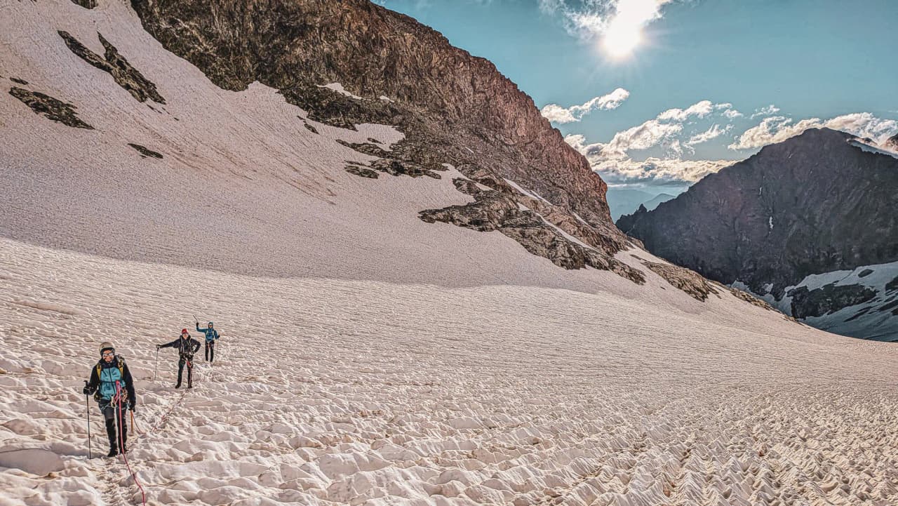 Trois alpinistes progressent sur un glacier des Écrins, sous un ciel ensoleillé et majestueux.