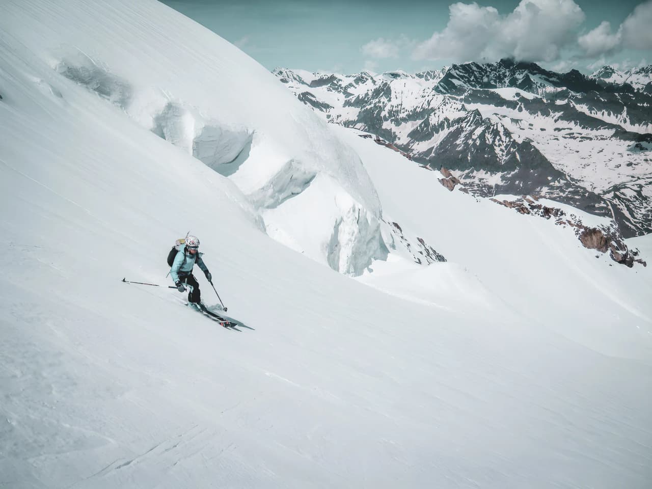 Skieur en pleine descente sur une pente enneigée, avec des sommets majestueux en arrière-plan.