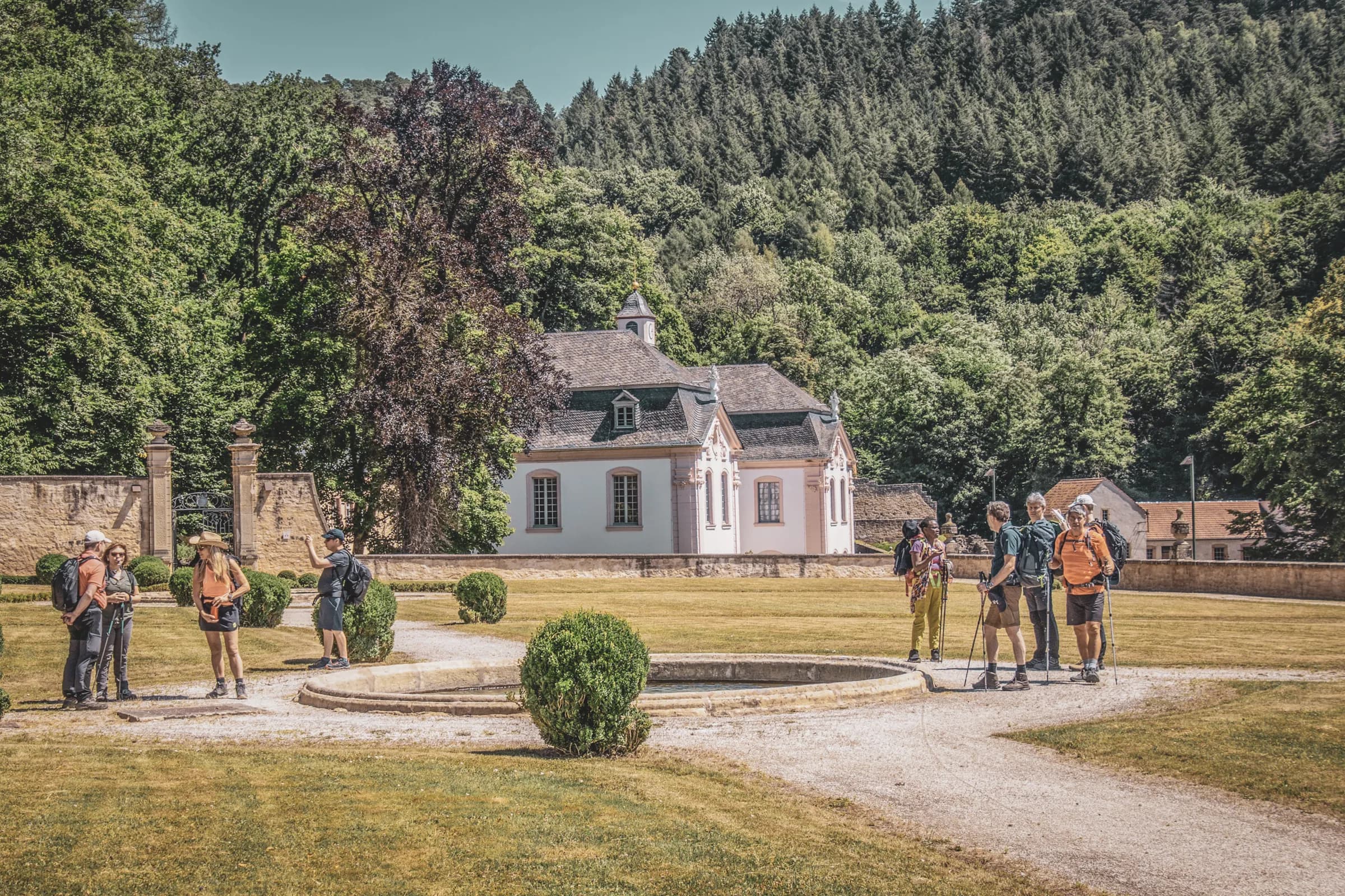 Groupe de randonneurs devant un charmant pavillon, entouré de verdure luxembourgeoise.