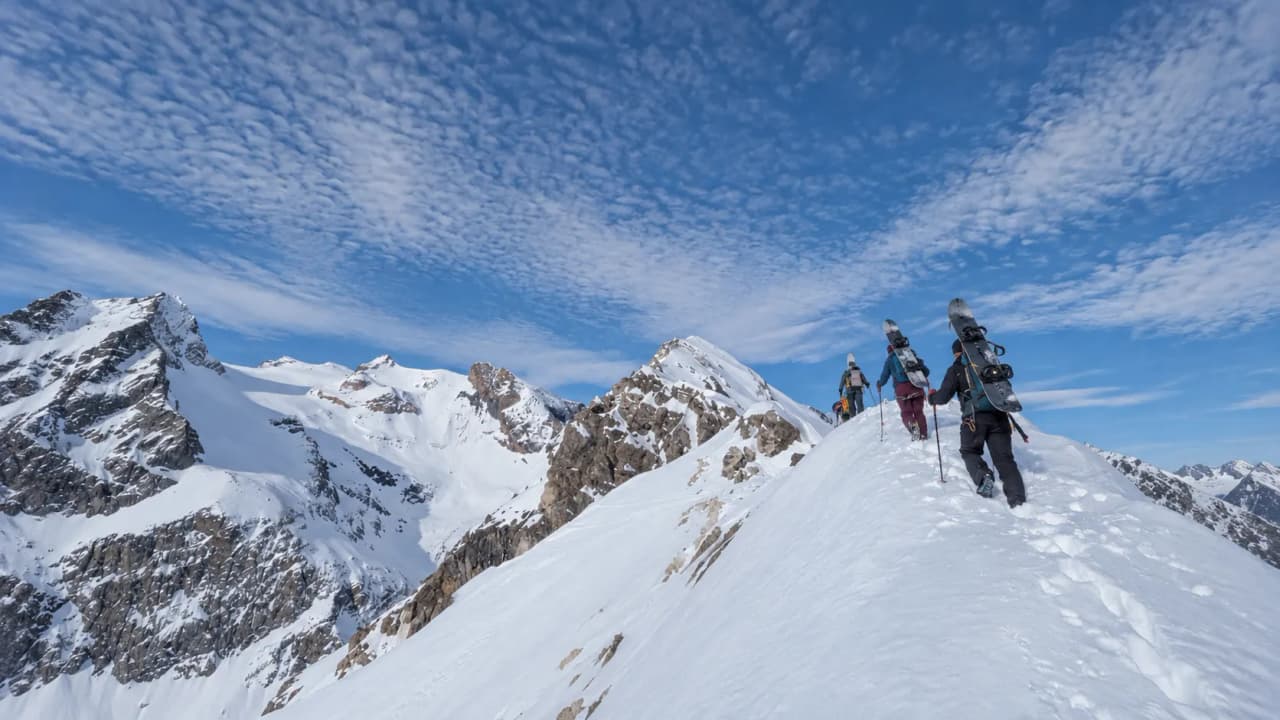 A group of splitboarders on the snow-covered summit in the Clarée Valley, under a blue sky.