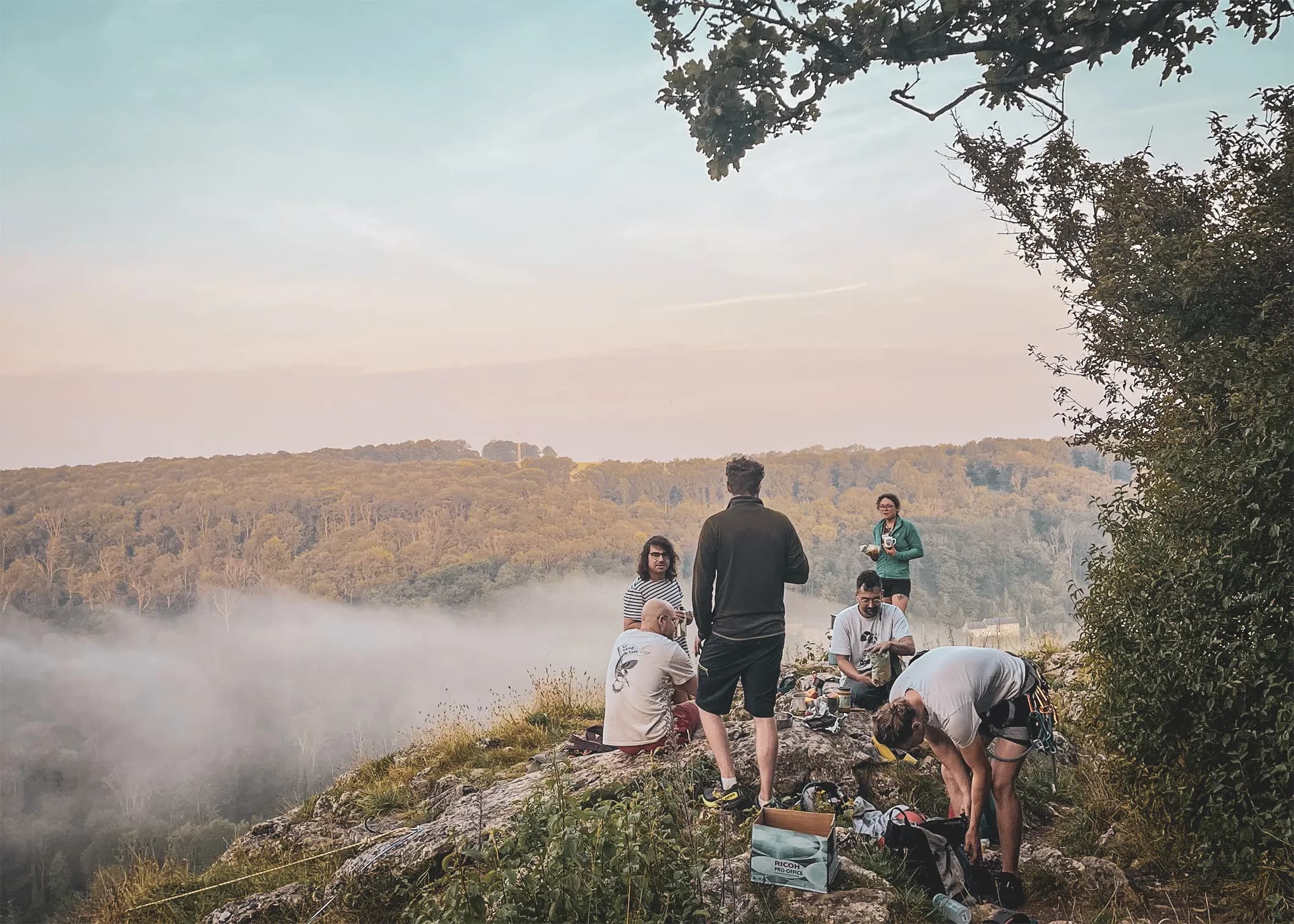 Groupe d'escalade surplombant la vallée brumeuse, ambiance conviviale au crépuscule.