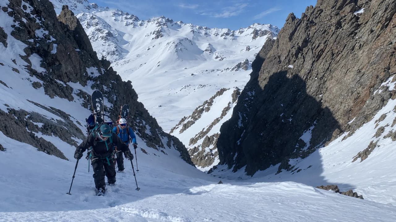 Hikers are making their way through the mountains, surrounded by majestic, snow-covered landscapes.