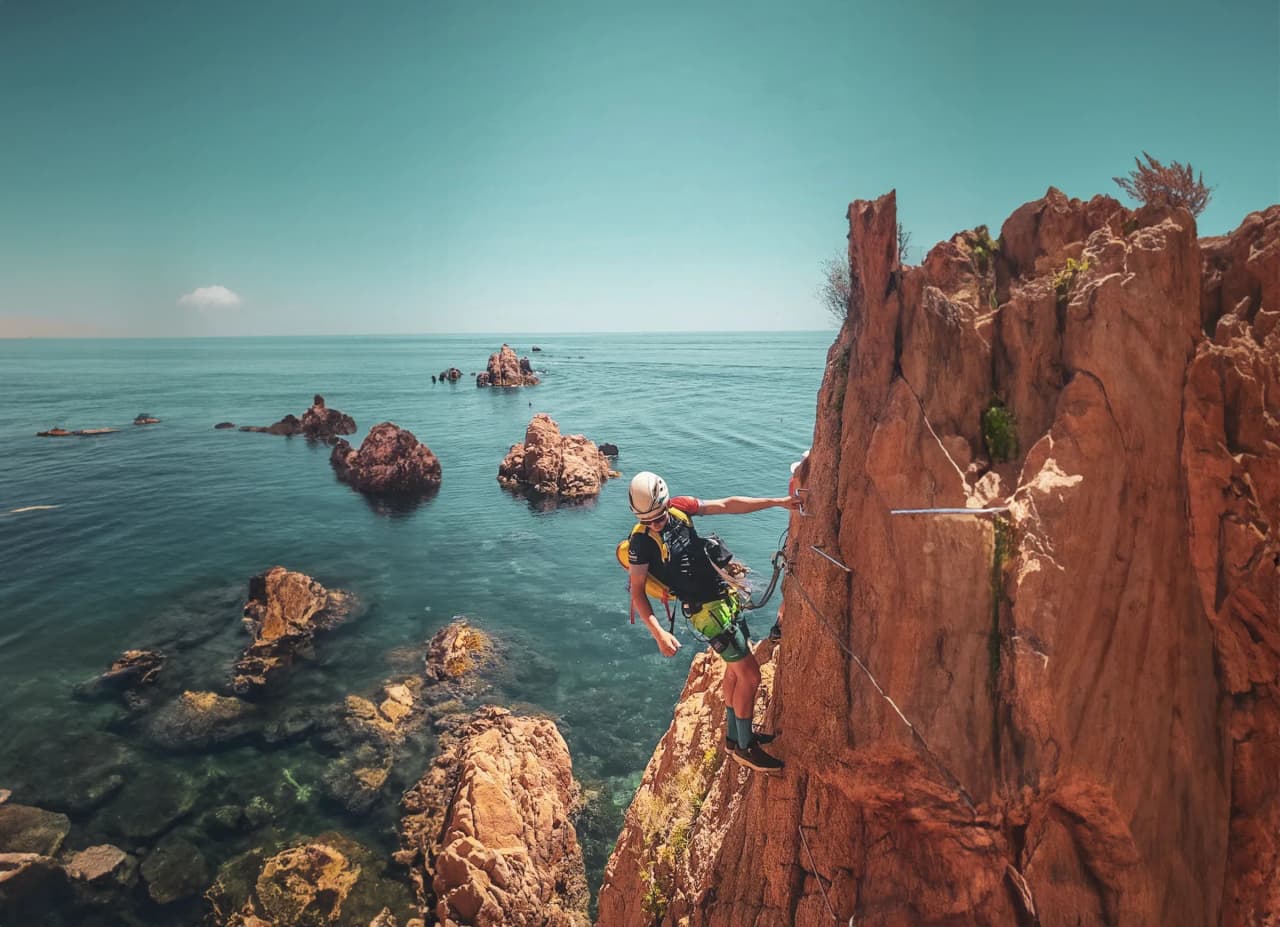 Un grimpeur s'aventure le long d'une falaise spectaculaire surplombant des eaux turquoise.