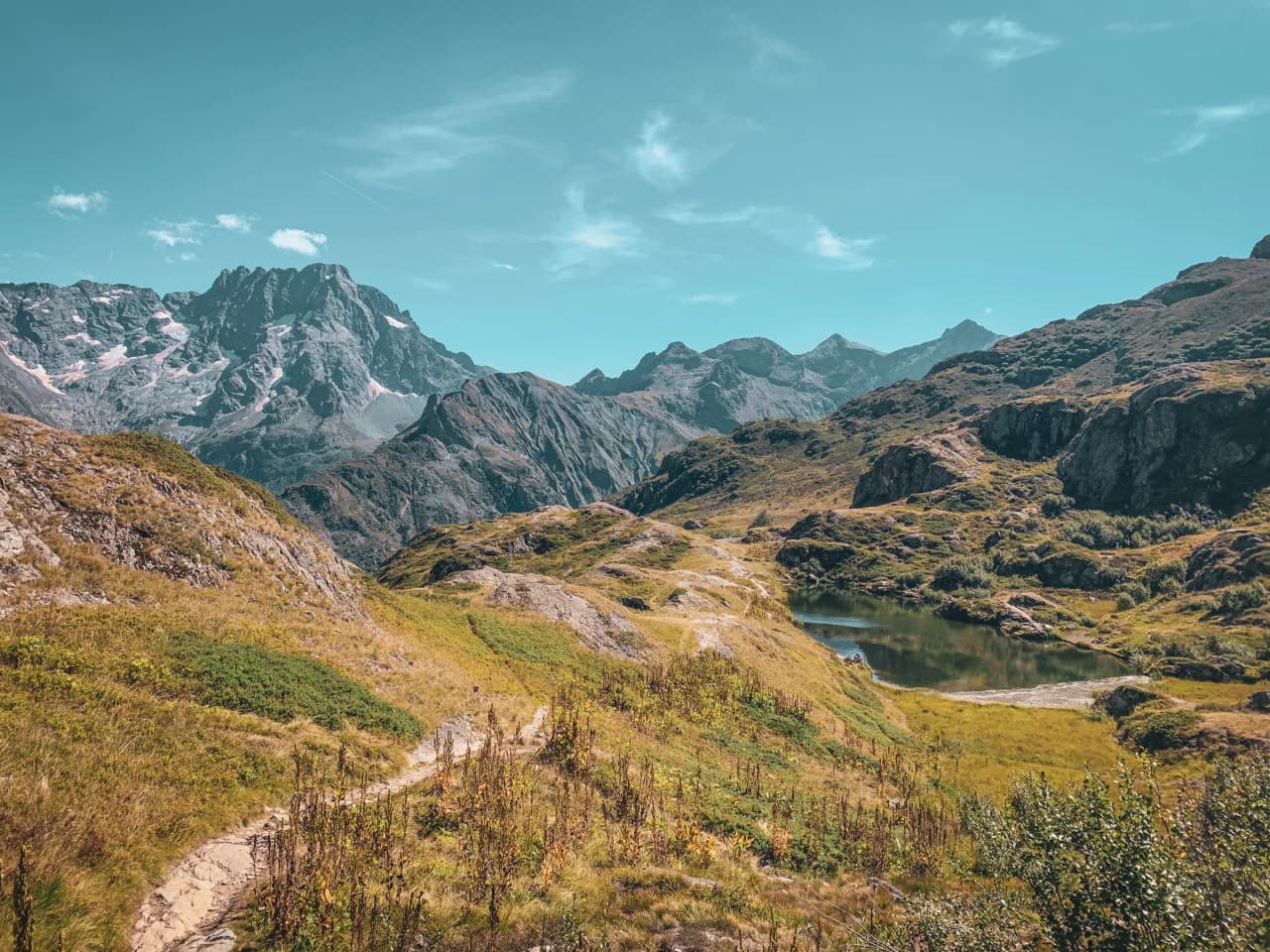 Lumière éclatante sur une vallée alpine verdoyante, lacs scintillants et montagnes majestueuses.