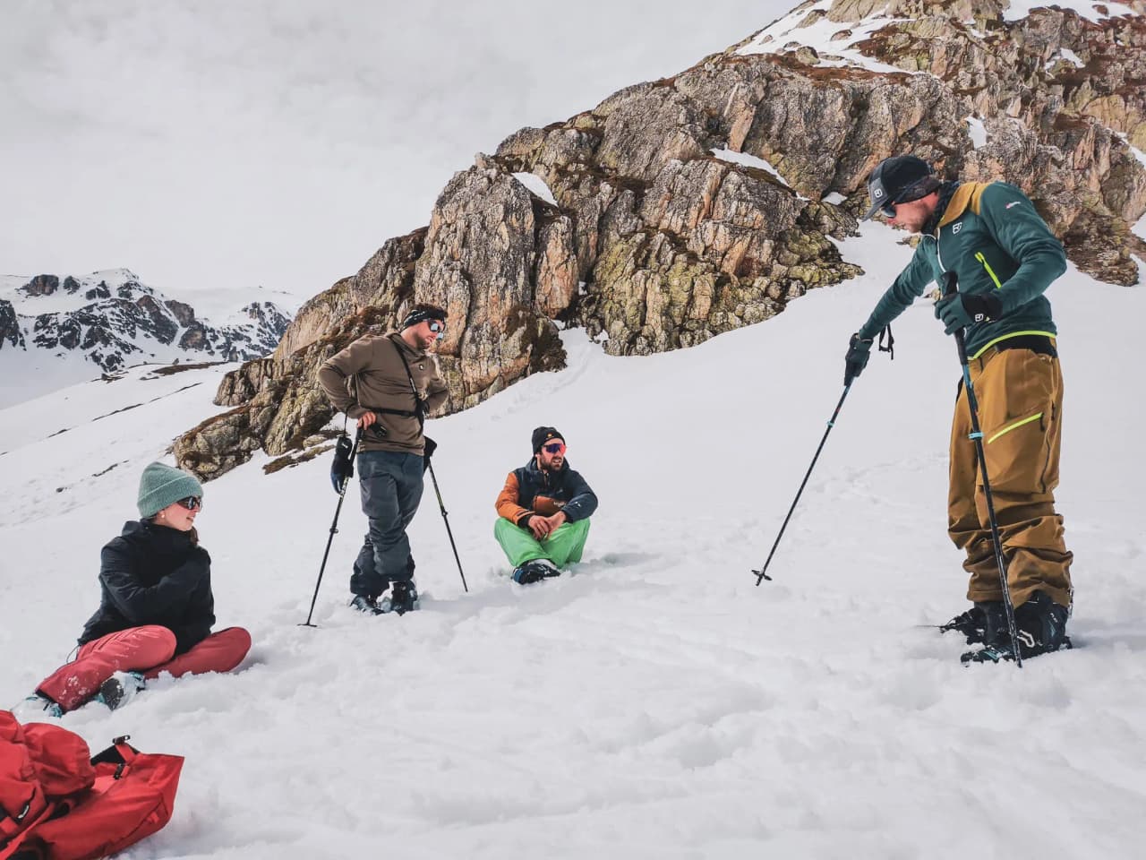Vier avonturiers genieten van een pauze midden in de sneeuw, omringd door majestueuze bergen.