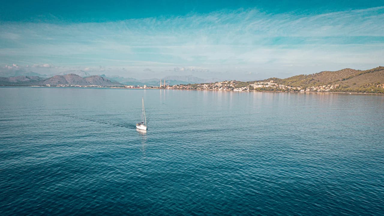 A sailing boat glides peacefully across turquoise waters, surrounded by the enchanting landscapes of the Balearic Islands.