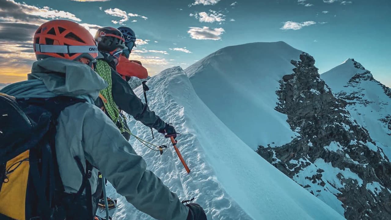 Trois alpinistes sur une crête enneigée, admirant un panorama majestueux à Chamonix.