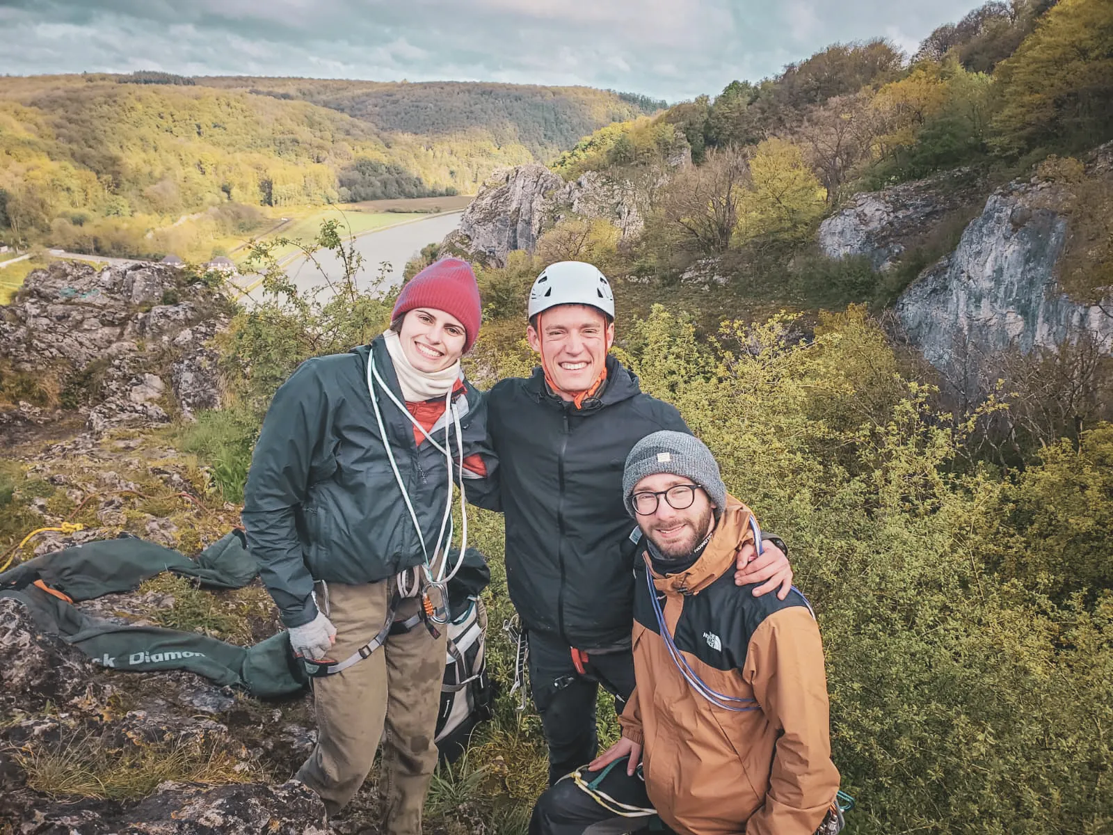 Trois amis souriants au sommet d'une falaise, prêts pour une aventure d'escalade en pleine nature.