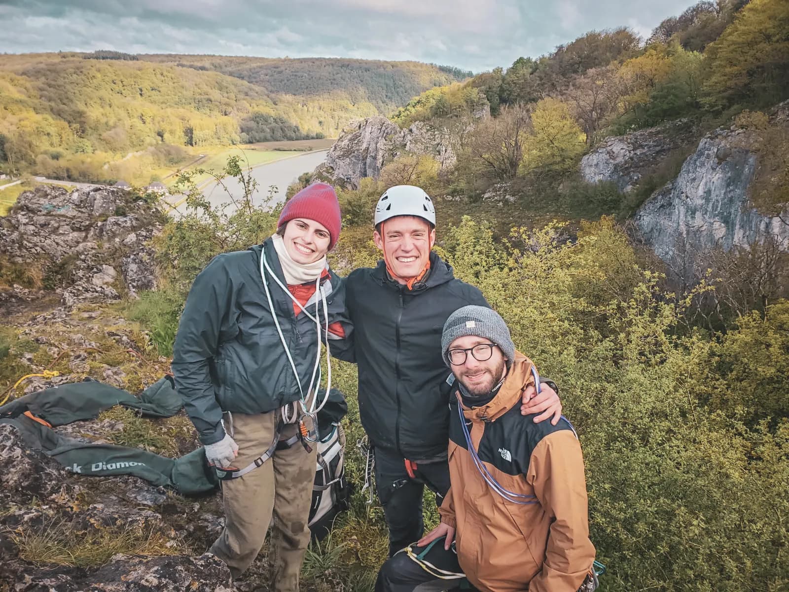 Trois amis souriants au sommet d'une falaise, prêts pour une aventure d'escalade en pleine nature.