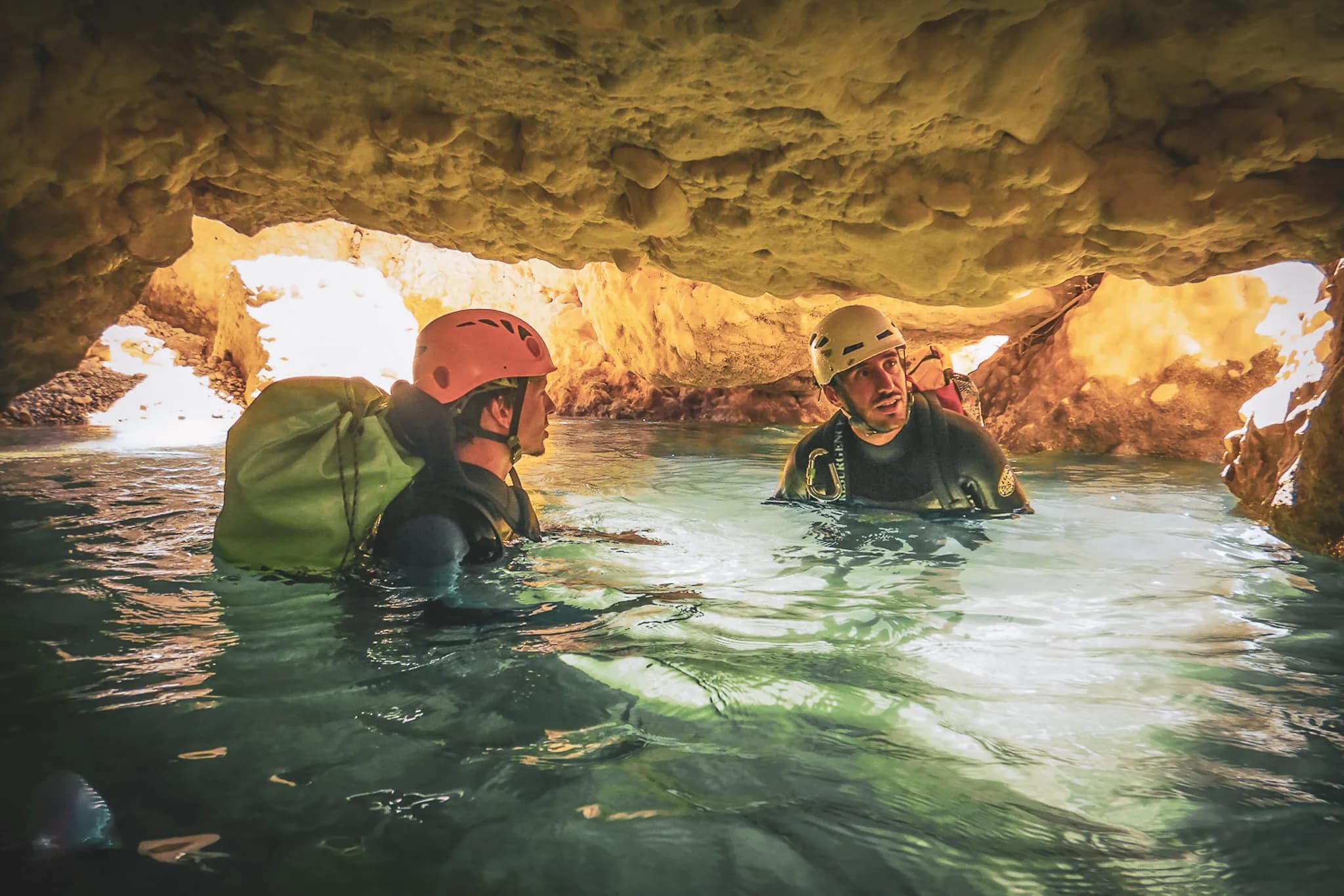 Two adventurers in neoprene suits explore watery gorges beneath a rocky ceiling.