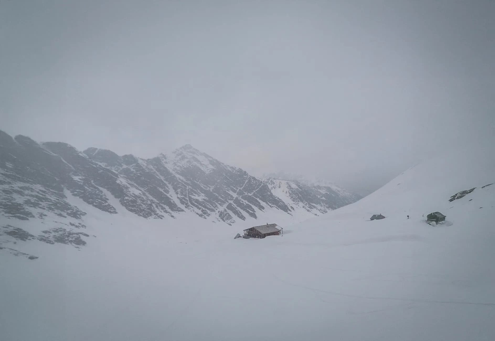 Un paysage hivernal majestueux, avec des montagnes enneigées et un refuge accueillant au milieu.