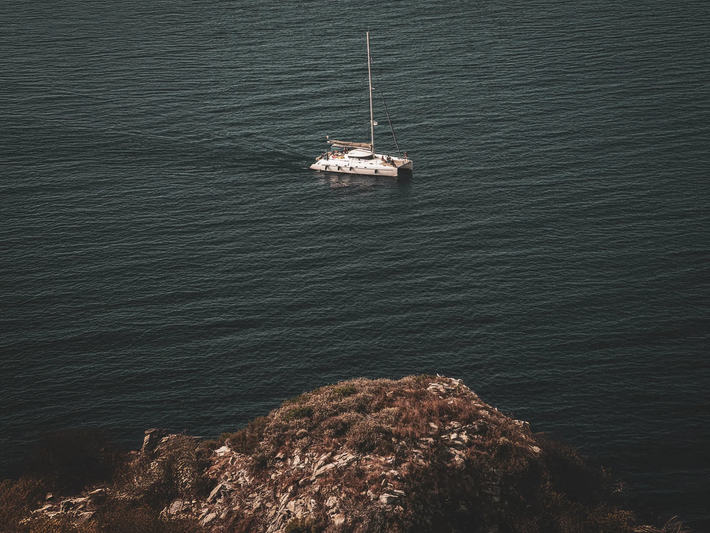 Un catamaran naviguant calmement sur les eaux turquoise près d'une côte rocheuse en Corse.