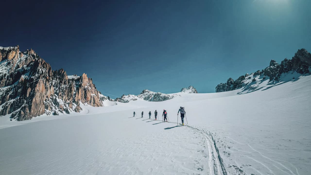 Group of skiers advancing on a glacier under a brilliant blue sky, majestic mountains in the background.