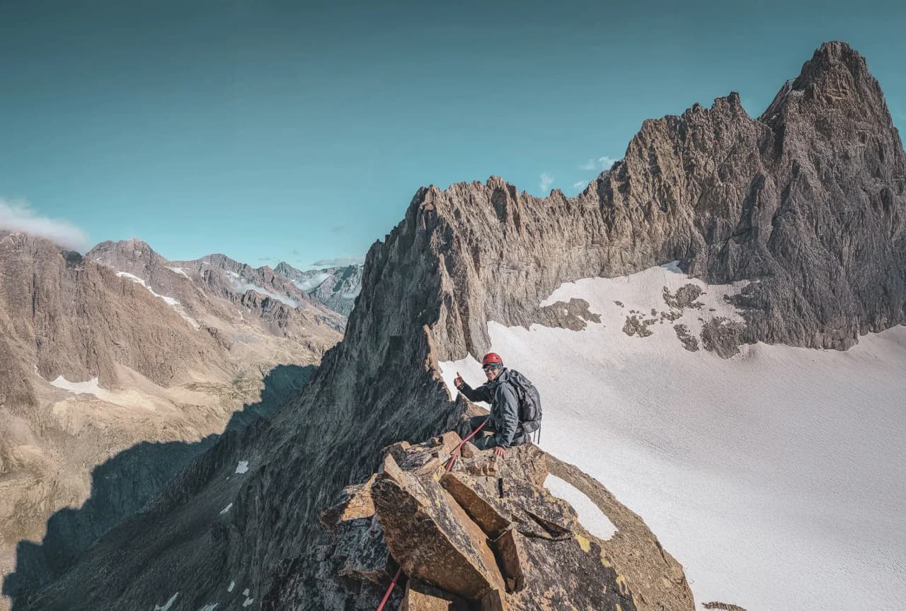 A mountaineer at the top of a rocky ridge, facing the majestic scenery of the Écrins.