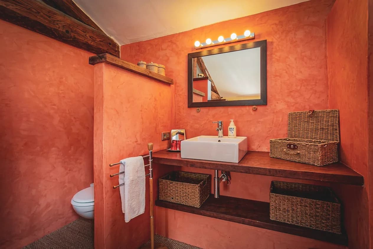 Salle de bain chaleureuse avec murs en terre cuite, lavabo moderne et touches rustiques.